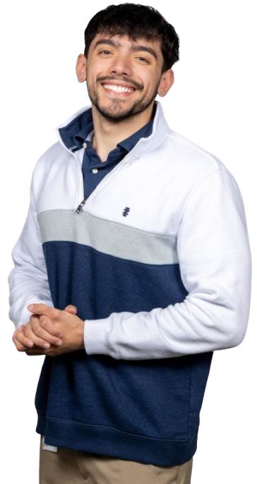 Smiling man with dark hair wearing a white, gray, and navy color-block pullover, standing with hands loosely clasped.